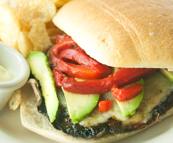 Grilled vegetarian sandwich topped with cheese, avocado and roasted peppers, plated with mayonnaise and potato chips