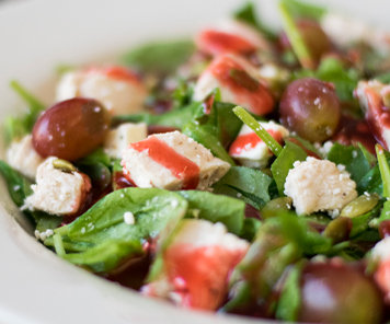 Close up of a salad with spinach, grilled chicken, and red grapes, topped with parmesan and a raspbperry dressing
