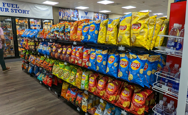 Shelves lined with chips, as well as frozen foods in the back freezers