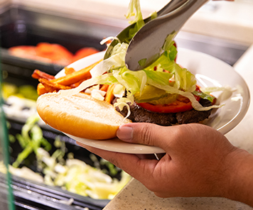 A customer putting toppings on their plated hamburger