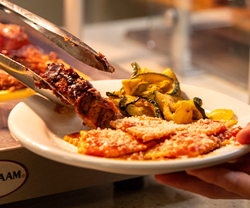 A customer being served a slice of beef to accompany their plated ravioli and grilled zucchini