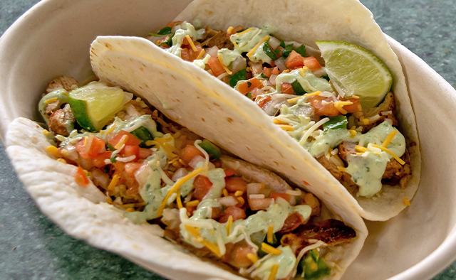 Chicken tacos topped with cheese, tomatoes, jalapeños, cilantro lime wedge and sauce