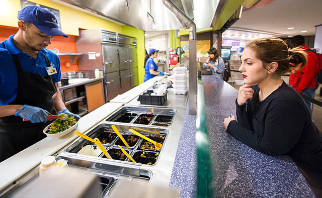 Student asking for burrito bowl toppings from the associate at the Guac & Roll counter