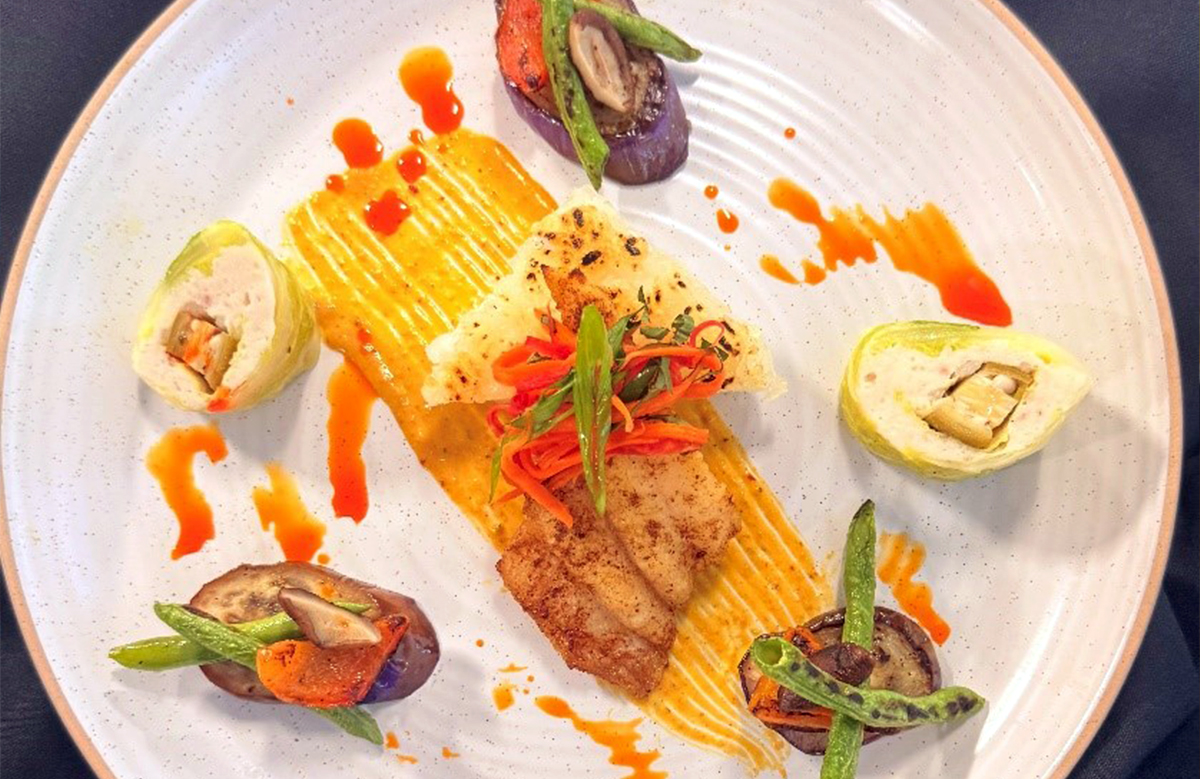 Chef Kaprishia's "Southeast Coasts" dish: catfish and okra stuffed napa cabbage with curry sauce, with a seared five-spice catfish over a crispy rice cake, topped with a pickled salad and served with sautéed vegetables.