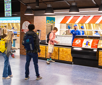 Student picking up his mobile order from 1846, while an associate waves hello to students behind him