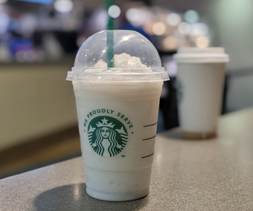 A vanilla bean frappe on a counter, with a hot drink in the background