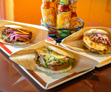 Trio of grilled arepas in front of hot sauces: black bean arepa, fire braised chicken arepa and breakfast arepa with fire braised chicken