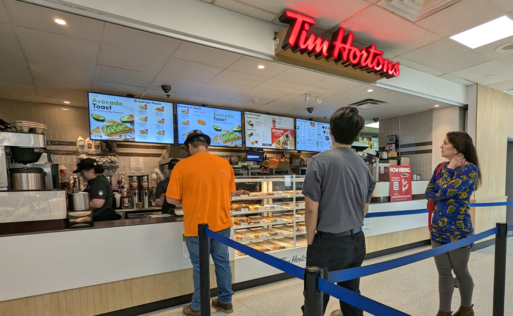Students lining up to order from the Tim Hortons counter; digital menuboards behind the associates