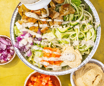 Noodle bowl with zucchini, chicken, onions, tomatoes and hummus