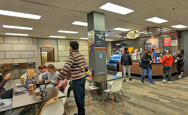 View of students sitting at a table eating and drinking their coffees on the left, with students odering at Whispers Abbott on the right