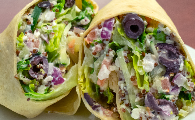 A veggie wrap with lettuce, olives, cucumbers, tomatoes, quinoa, onions and feta cheese