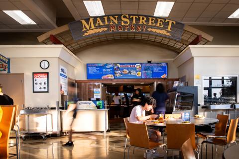Students dining and walking around at Goodyear Dining Center, where associates are at the register counter under the digital menuboard signs. Photo by Meredith Forrest Kulwicki.