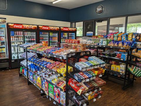 Shelves lined with snacks, and Coca-Cola coolers lined with drinks, in the back at Teddy's convenience store in Governors.