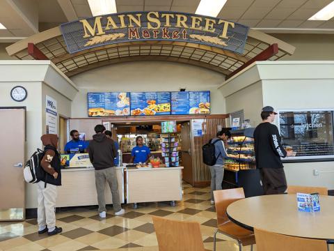 Students in line to order from Main Street Market at the same location as Goodyear Dining Center, with the digital menuboard signs behind the associates.