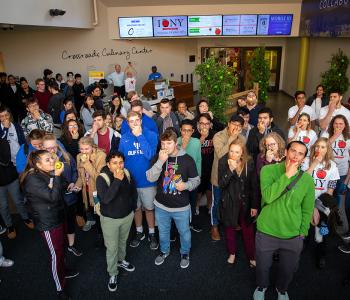 Students and staff biting into apples in the lobby at the Apple Event at Crossroads Culinary Center (C3) in Ellicott Complex on North Campus