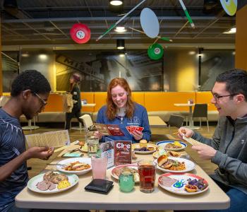 Students discussing their Clue game progress while eating their special dinners