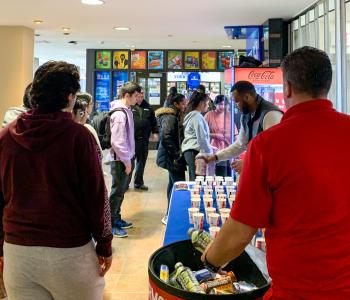 Students lining up to use the Coke claw machine and staff setting up free drinks at the table