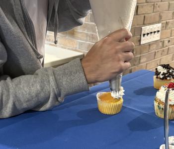 Student piping frosting onto a cupcake