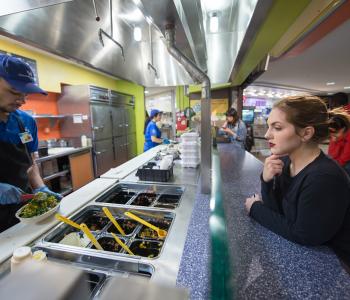 Student ordering from an associate at the Guac & Roll counter in Ellicott Food Court. Photo by Onion Studio.