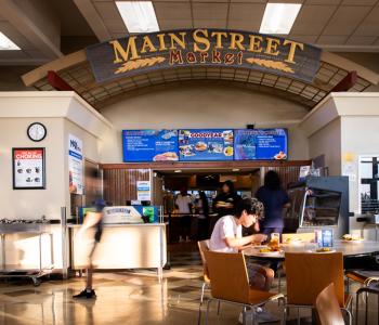 Students dining and walking around at Goodyear Dining Center, where associates are at the register counter under the digital menuboard signs. Photo by Meredith Forrest Kulwicki.