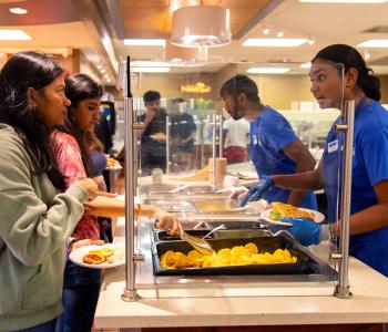 Students talking with an associate as they are pointing and talking about the buffet food in front of them. Photo by Meredith Forrest Kulwicki.