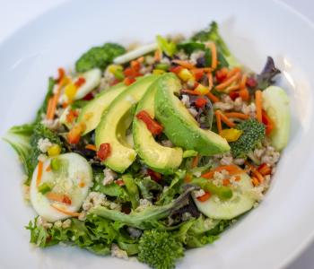 A salad consisting of Edgy mix, avocado, peppers, broccoli, cucumbers, quinoa, carrots, and diced onion.