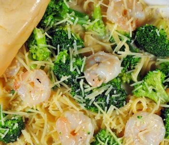 Closeup of linguine with broccoli and shrimp, topped with alfredo sauce and parmesan cheese, served with a breadstick.