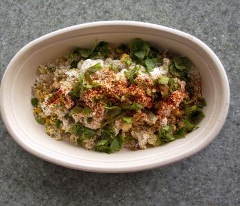 Burrito bowl topped with cheese, sour cream, corn, and cilantro.