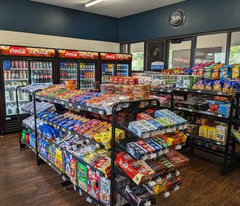 Shelves lined with snacks, and Coca-Cola coolers lined with drinks, in the back at Teddy's convenience store in Governors.