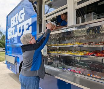 Big Blue food truck parked on South Campus. A customer is receiving her order from an associate.