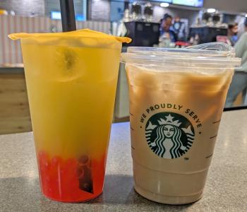 An iced yellow bubble tea drink with strawberry bursting boba pearls next to an iced coffee on the Perks waiting counter.