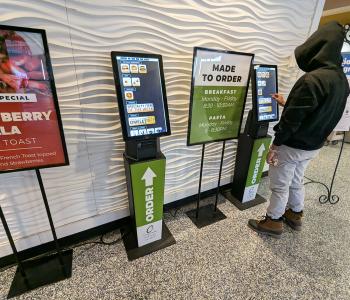 Two ordering kiosks at the front of C3, one of which a student is ordering breakfast from.