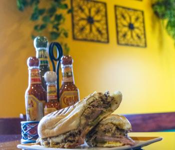A Cuban sandwich with the hot sauce center piece and the wall decorations behind it.