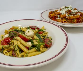Caprese pasta and rigatoni campagnolo plated next to each other in white dishes.