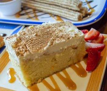 A piece of tres leches cake with strawberries on a plate, and plated churros behind it.