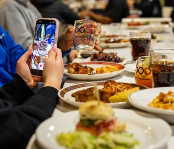 Student taking a photo on their phone of the commemorative glass alongside international food at the event. Photo: Meredith Forrest Kulwicki